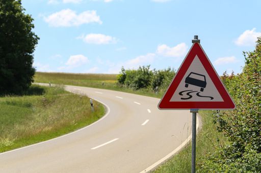 Slippery road - Road sign stands on a sharp turn.