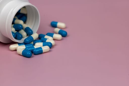 A close-up shot of blue and white pills scattered from a plastic jar