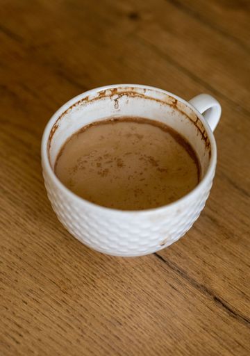 A close-up shot of coffee with milk in a cup on a wooden table