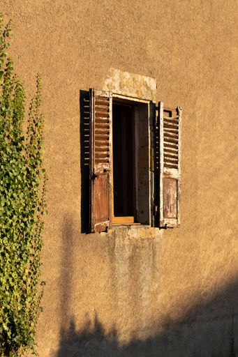 A vertical shot of an abandoned buildings with an old window with shutters