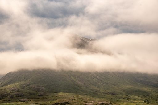 A beautiful green mountain covered in the white fluffy clouds