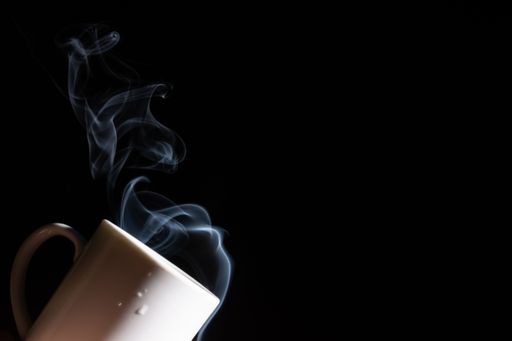 A closeup of a white cup against a black background with smoke coming out of it