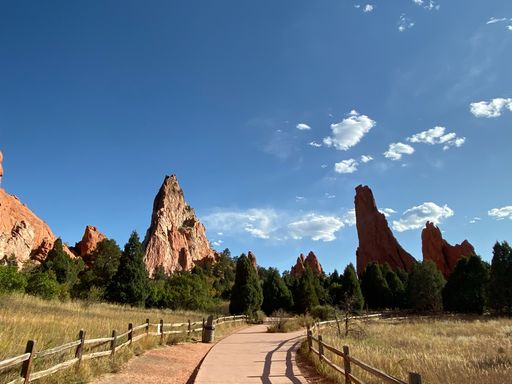 A path surrounded by big rocks raising above a forest on a sunny day