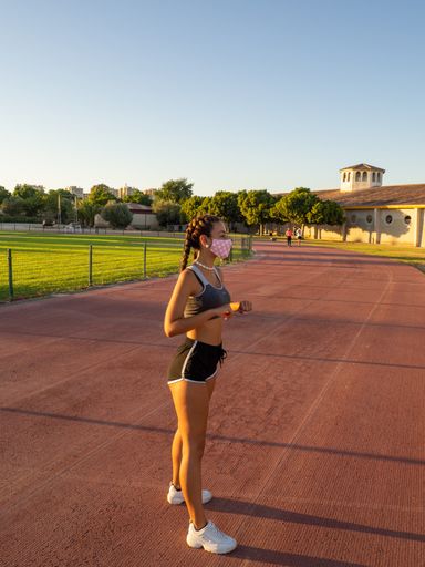 An athletic Caucasian female in a gym outfit with a medical mask working out outdoors - the new normal after covid-19