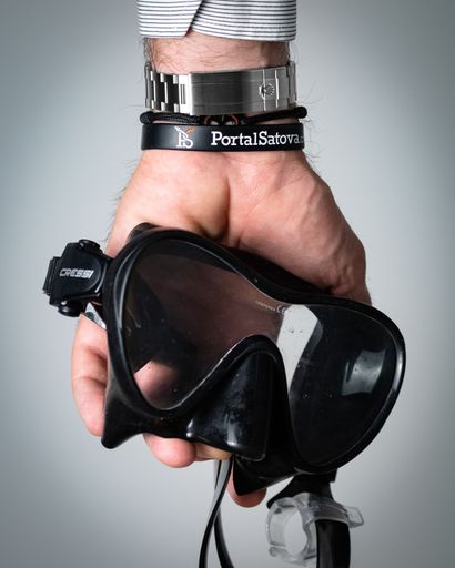 A vertical shot of the man's hand wearing Rolex Explorer and holding a black swimming goggles