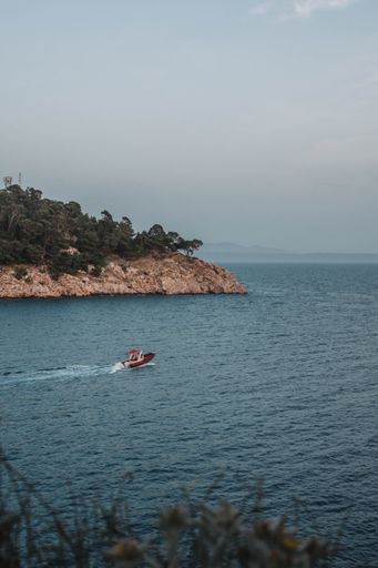 A vertical shot of people riding a motorboat in a blue sea near a  cliff with green trees