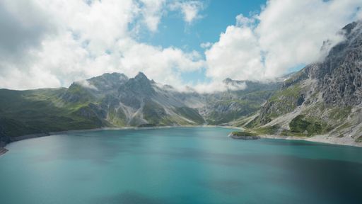 A breathtaking scenery of a tranquil lake in the grass covered mountains against a cloudy sky