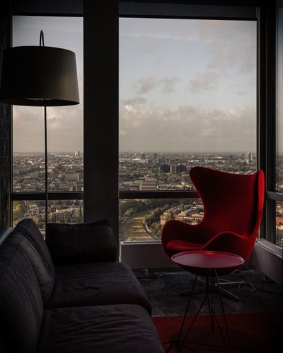 A vertical shot of a red armchair next to the window of an apartment on a high floor and the scene of the city from the window