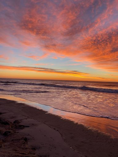 A vertical shot of a sandy beach and the sea captured at a beautiful sunset