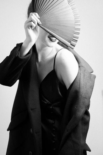 A vertical greyscale shot of an attractive female posing with a fan