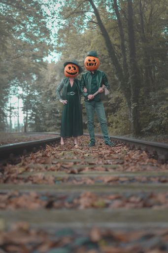 A vertical shot of a couple wearing pumpkins on their heads in the forest