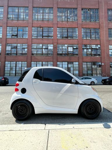 A small white car parked on the street with a building in background