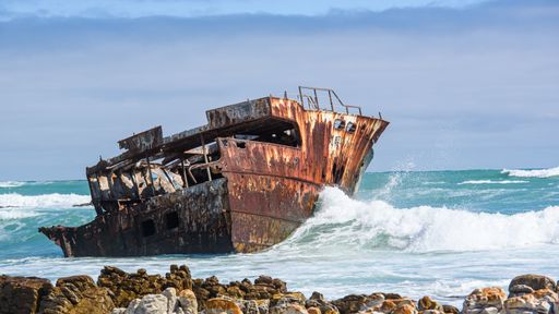 A closeup of an abandoned rusty ship on the sea with water waves and gloomy sky in the background