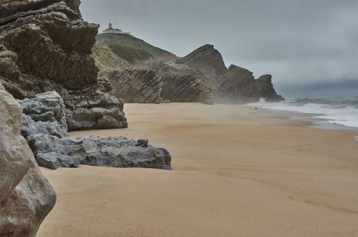 Rocks formations on the sandy beach in Figueira da Foz, Portugal by water under stormy gray sky