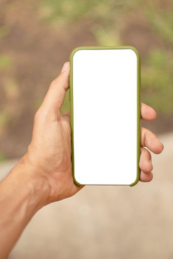 A vertical close-up shot of a man holding a smartphone in his hand with a white screen in a garden