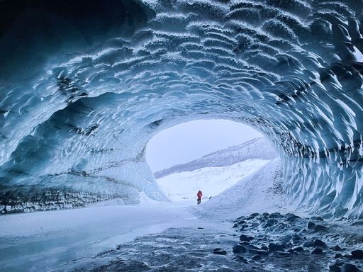 A scenic view of a man entering a cave covered in ice during a beautiful winter day in Fairbanks