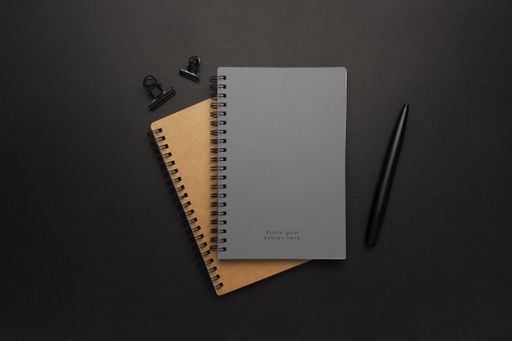 A top view of notebooks and a pen on a black surface