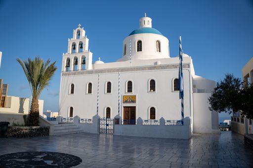 A high angle of a Blue Domed church with blooming trees, blue, cloudy sky background, Santorini