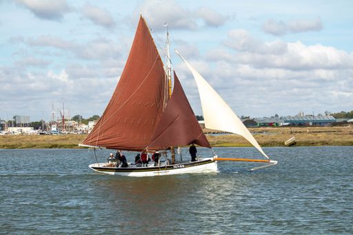 A sailboat floating on a river with the cloudy sky in the background