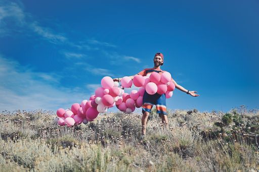 A Caucasian man surrounded with a string of pink balloons while standing on a mountain