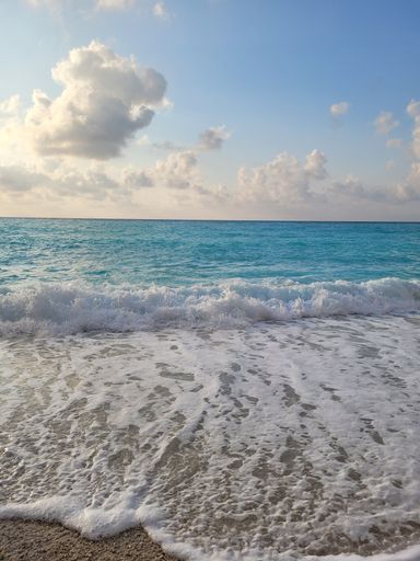 A beautiful scenery of foam waves on sandy beach under blue sky on sunny day