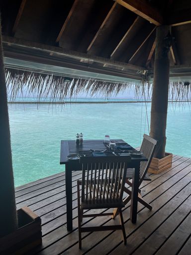 A vertical shot of a table with chairs set up on a wooden pier with a beautiful view of the sea