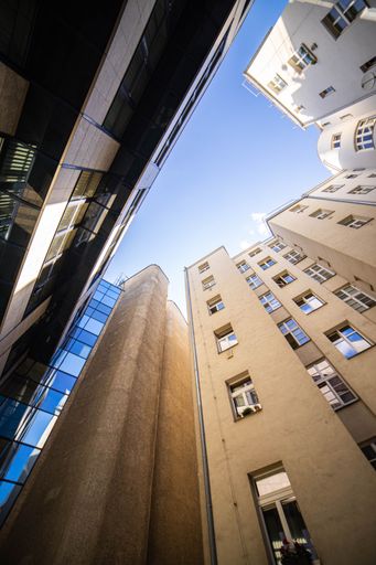A vertical low-angle view of tall buildings with windows under a blue sky during the day