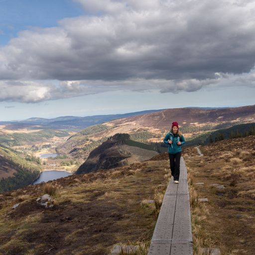 The woman on a narrow boardwalk against the background of mountains. Glendalough, Wicklow, Ireland.
