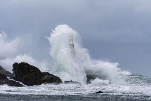 A tall lighthouse in the stormy ocean under dark storm clouds