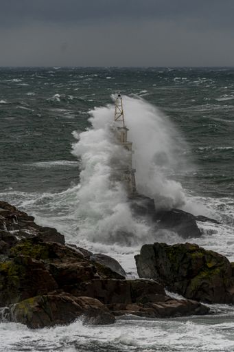A tall lighthouse in the stormy ocean under dark storm clouds