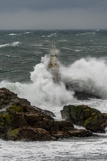 A tall lighthouse in the stormy ocean under dark storm clouds