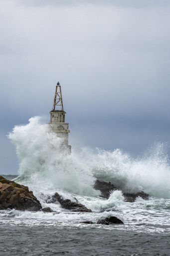 A tall lighthouse in the stormy ocean under dark storm clouds