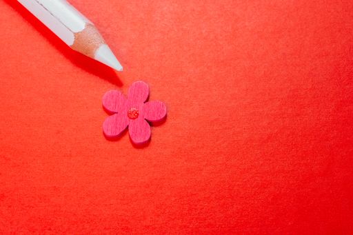 A closeup top view maco shot of an artificial flower next to a pencil