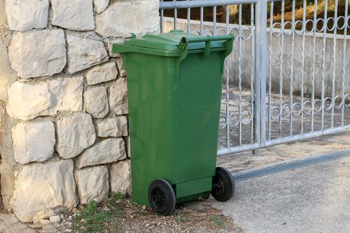 A green trash can by the gates of the house