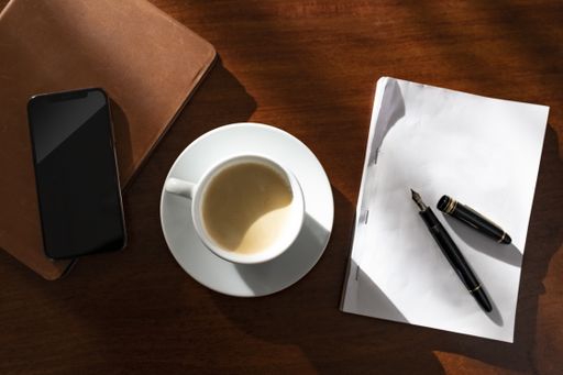 A high angle shot of a table of a writer with a paper pen and a cup of coffee