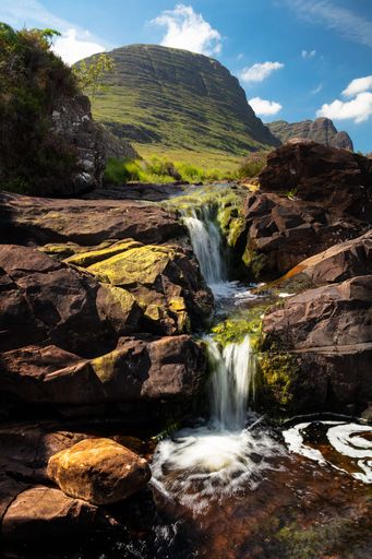 A vertical shot of the flowing rocky North Coast 500 waterfall in the Scottish Mountains
