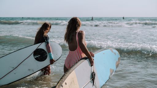 Two female surfers holding their surfboards and walking to the sea