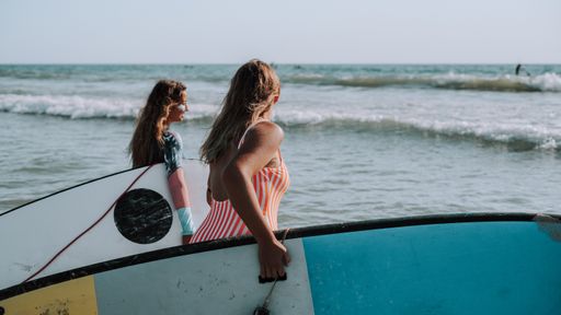 Two female surfers holding their surfboards and walking to the sea