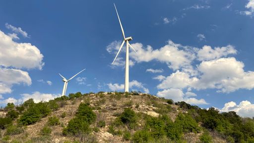 A low angle shot of windmills on top of green hills against a cloudy blue sky