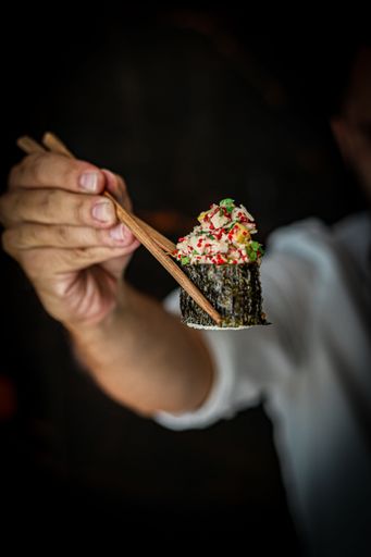 A vertical shot of a person holding a sushi with sticks