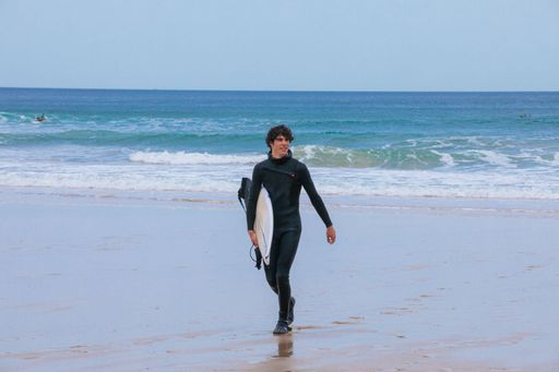 A Caucasian male coming back from surfing in the ocean