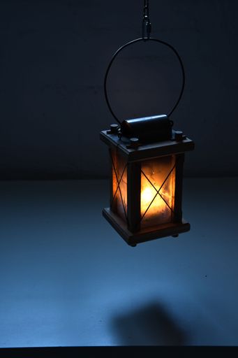 A vertical closeup of a lit retro lantern, lamp hanging from above