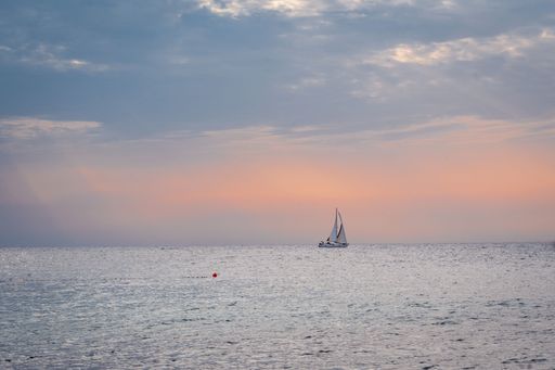 A sailboat in the sea with a beautiful orange sunset in the background