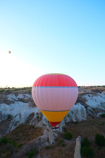 A vertical shot of a striped hot air balloon flying over Cappadocia, Turkey