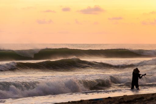 Lonely fisherman in the big waves during amazing sunset