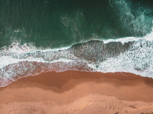 A top view of splashing sea waves with sea foam on a sandy shore