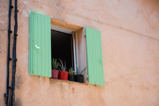 A low angle shot of a green window decorated with flower pots