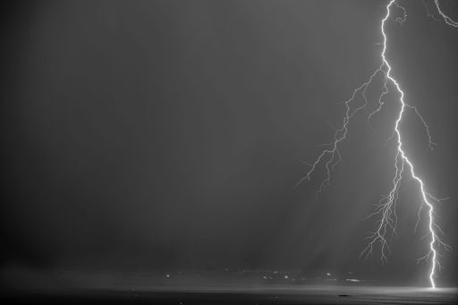 A black and white of a lightning and storm clouds over the sea and the city.