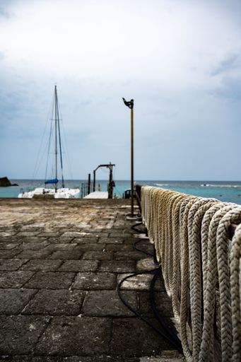 A selective focus shot of ropes on the metal railing of the pier by the sea on a cloudy day