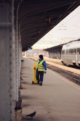 A worker cleans up a yellow trash bin at a train station